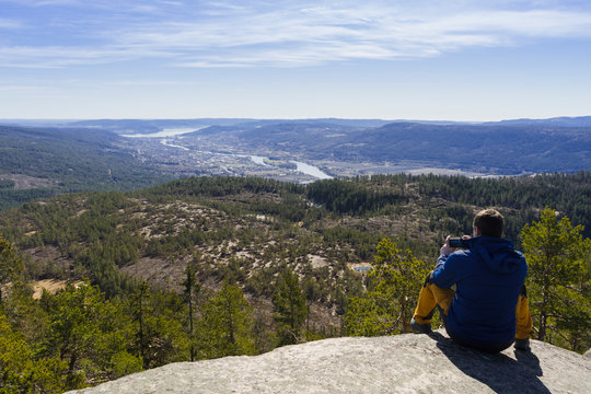 Man taking picture of nature and a city far away.