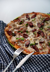 Pizza on the table with place for text. Checkered napkin, knife and vinca. Bavanese pizza with sausages and herbs. Food at home.
