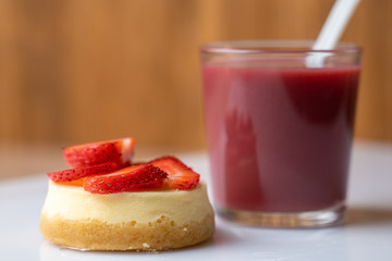 A slice of strawberry cheesecake with a nice raspberry drink in a glass on a white table