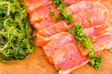 Fish platter on a wooden board. Lightly salted salmon, chuka salad and green onion decor