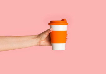 Millennial girl holding reusable eco cup with hot beverage on pink background, close up
