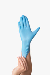Obraz premium Infectious disease protection. Young female putting on blue medical glove against white background, closeup