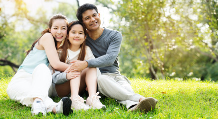 Asian families sit for a picnic at the park. Parents and daughters hug And happy smile. Resting...