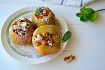 Baked apples filled with walnuts and dried apricots on a white wooden background.