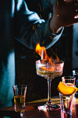 Male bartender holds fired up sugar above delicious alcohol cocktail