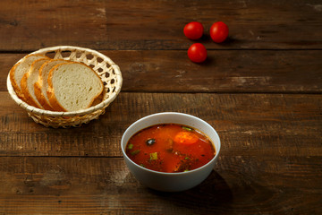 A plate of Italian tomato soup with potatoes and mushrooms on a wooden table and bread.