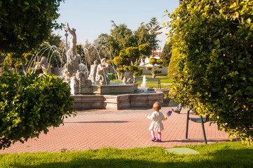 Fototapeta na wymiar Toddler girl walking in the park with a colorful toy windmill in hand. First steps. Family outing.