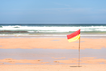 a flag waving.
a red yellow flag waves in front of the ocean. alert, message.