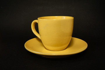 Yellow coffee cup and saucer on a black background.