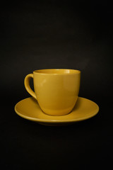 Yellow coffee cup and saucer on a black background.