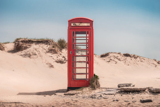 Fototapeta A vintage red telephone box in the sand dunes of a deserted beach near Sandbanks, Studland, Dorset, England, UK