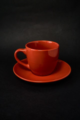 Red cup of coffee and saucer on a black background.