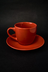 Red cup of coffee and saucer on a black background.