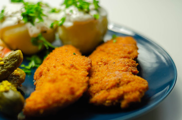 Breaded and herbed chicken breast fillet served with mashed potatoes,  tomato salad with onions and gherkin