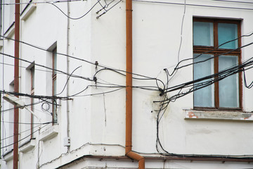 The plastered facade of an old house. Plenty of entangled electrical wires near windows and a drainpipe. Problems of ill-conceived electrical wiring