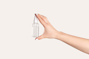 Viral infection prevention. Young woman holding bottle with sanitizer on light background, close up