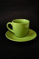 Green cup of coffee and saucer on a black background.