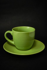 Green cup of coffee and saucer on a black background.