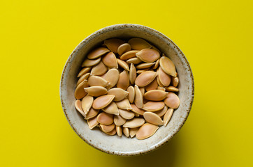 Pumpkin seeds in bowl on yellow background. Gourd seeds.