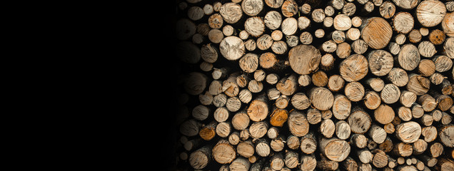 Stack of firewood with black free space for text on the left. Wooden background with logs.