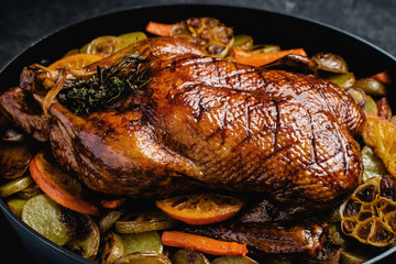 Whole Duck Roasted with Oranges, Carrots and Potatoes on Dark Stone Background