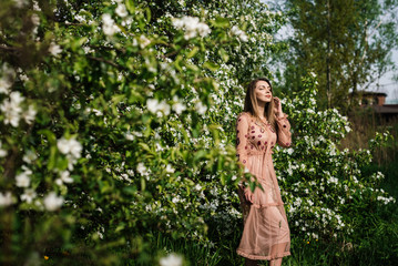 beautiful girl in a dress with her eyes closed enjoys the warmth of the sun against a background of white flowers in a flowering garden