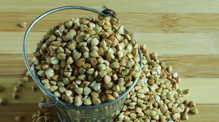 Small metal bucket with raw buckwheat on a board on a brown background. Organic vegetarian food. The concept of a healthy and balanced diet. Dietary nutrition. Copy space. Top view.