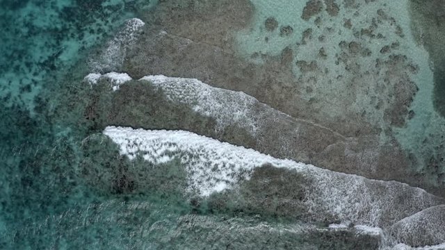 Aerial backwards shot of waves splashing shore at beach, drone flying over sea - Coco Plum Cay, Belize