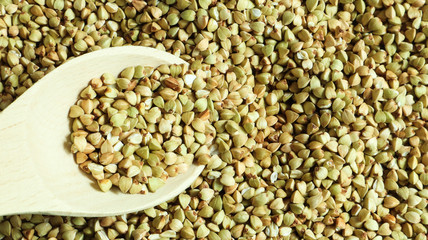 Buckwheat scattered background, raw green cereal in a wooden spoon. Healthy groats. Organic raw non-fried vegetarian food. The concept of a healthy and balanced diet. Diet product. healthy groats.