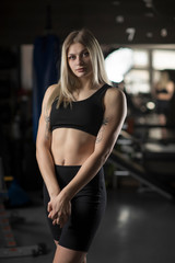 Obraz na płótnie Canvas Portrait of a young girl, a fitness trainer in a dark sports uniform with a gym.