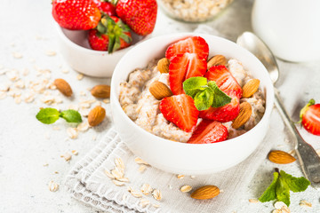 Oatmeal porridge with fresh strawberry and nuts on white background.