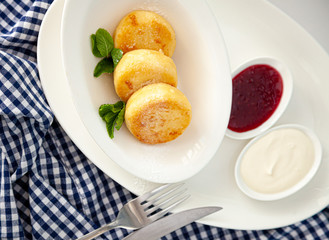 Round curd cheesecakes. Serving homemade food on a white plate. Cheesecake with mint for breakfast, a serving of three. High calcium appetizing healthy food. White plate. Mint. Checkered napkin, fork.