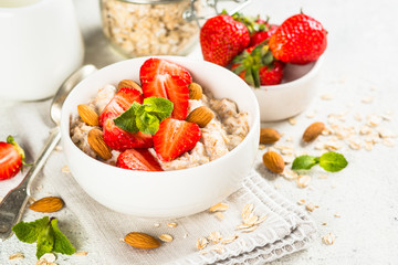 Oatmeal porridge with fresh strawberry and nuts on white background.