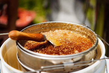 Natural raw honey being processed through a strainer to filter our bees wax.