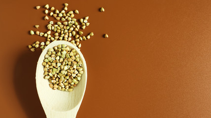 Green buckwheat in a wooden spoon on a brown background. Great food. healthy groats. Organic raw non-fried vegetarian food. The concept of a healthy and balanced diet. Dietary foods. Copy space