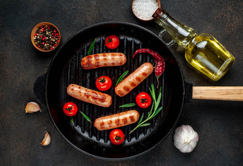 classic grilled sausages and tomatoes with spices in a cast-iron grill pan on a stone background