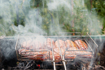 BBQ with fiery sausages on the grill. Raw sausages cevapcici grilled ha open fire on the street. Selective focus