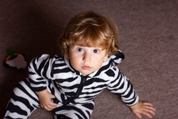 A child in a zebra costume. Little boy is playing in a dark room. Baby in pajamas.