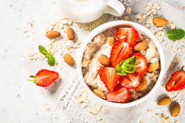 Oatmeal porridge with fresh strawberry and nuts on white background.