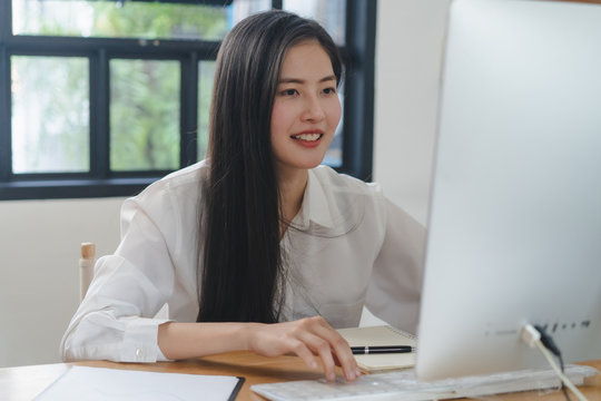 Working from home using internet communication concept. Asian young woman wear earphones talking  in video conference with business partners and worker team via online internet at her home.