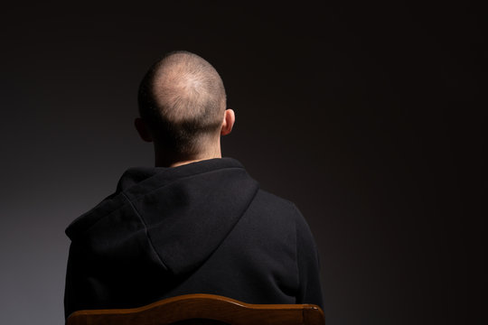 Back view of casual bald young man in black hoodie isolated on dark background with copyspace