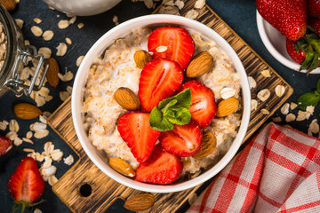 Oatmeal porridge with fresh strawberry and nuts on dark background.