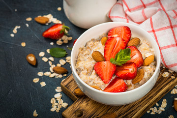 Oatmeal porridge with fresh strawberry and nuts on dark background.