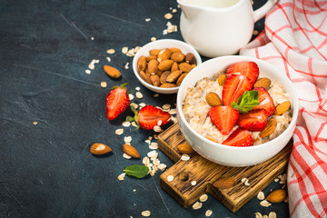 Oatmeal porridge with fresh strawberry and nuts on dark background.