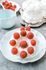 Delicious mini Pavlova meringue cake decorated with fresh raspberries, with a beautiful Cup lying on a platter