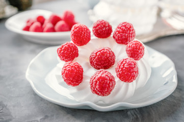 Delicious mini Pavlova meringue cake decorated with fresh raspberries, with a beautiful Cup lying on a platter