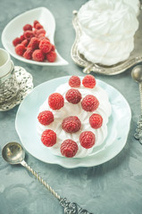 Delicious mini Pavlova meringue cake decorated with fresh raspberries, with a beautiful Cup lying on a platter