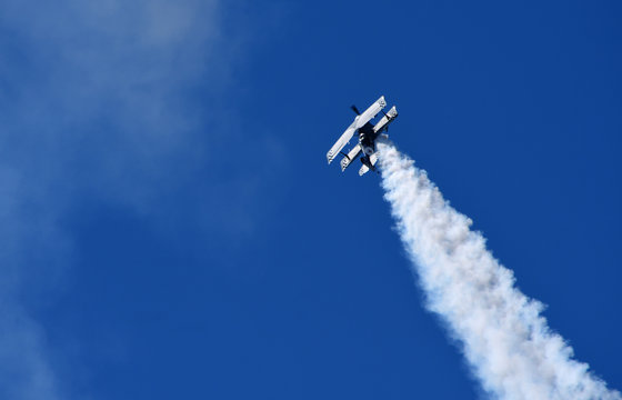  Pitts Model 12  stunt byplane  with smoke trail and blue sky.