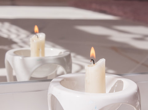 Burning candle in mirror reflection in a white candlestick. The concept of a sessional session and fortune telling