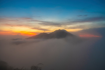 A cinematic magical horizon view of kintamani volcano peak and golden sky from the top of the Mount Batur during the sunrise with fog